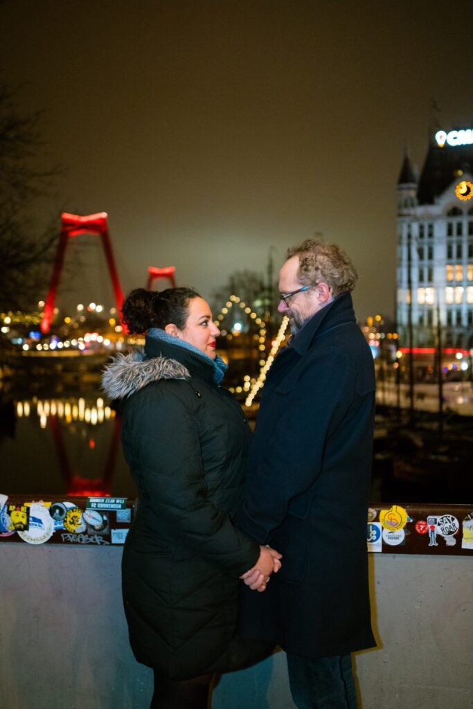 Paul en Amoorah poseren bij nacht in de Oude Haven in Rotterdam. Op de achtergrond zie je de Willemsbrug en het Witte Huis.